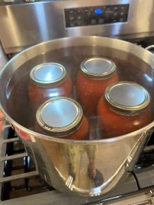 tomatoes in jars simmering in a pot on the stove